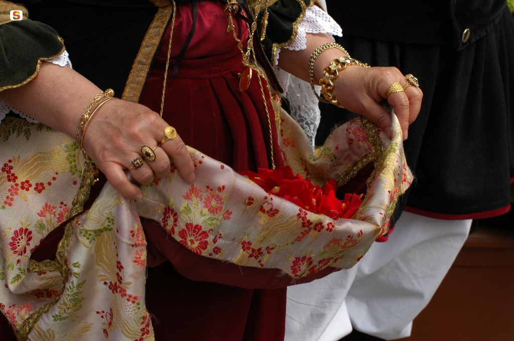 Donna in abito tradizionale si prepara a spargere i petali per sa ramadura